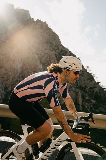 Rick Zabel mit Helm und gestreiftem Trikot fährt auf einem weißen Rennrad an einem Gebirgsabhang entlang