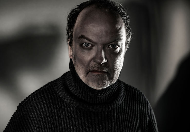 Jens Wawrczeck mit lockigem Haar trägt einen schwarzen, grob gestrickten Rollkragenpullover vor unscharfem Hintergrund