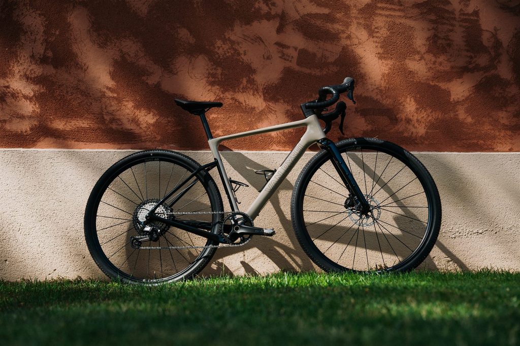 Beiges Van Rysel EDR-G Gravelbike vor einer rotbraunen Wand
